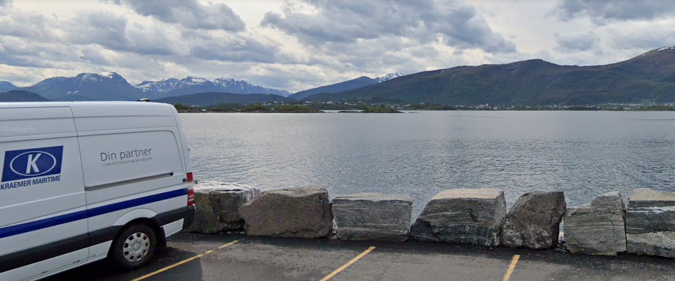 Image d’un camion stoppé sur un parking à côté d’un cours d’eau, des montagnes son visible en arrière-plan